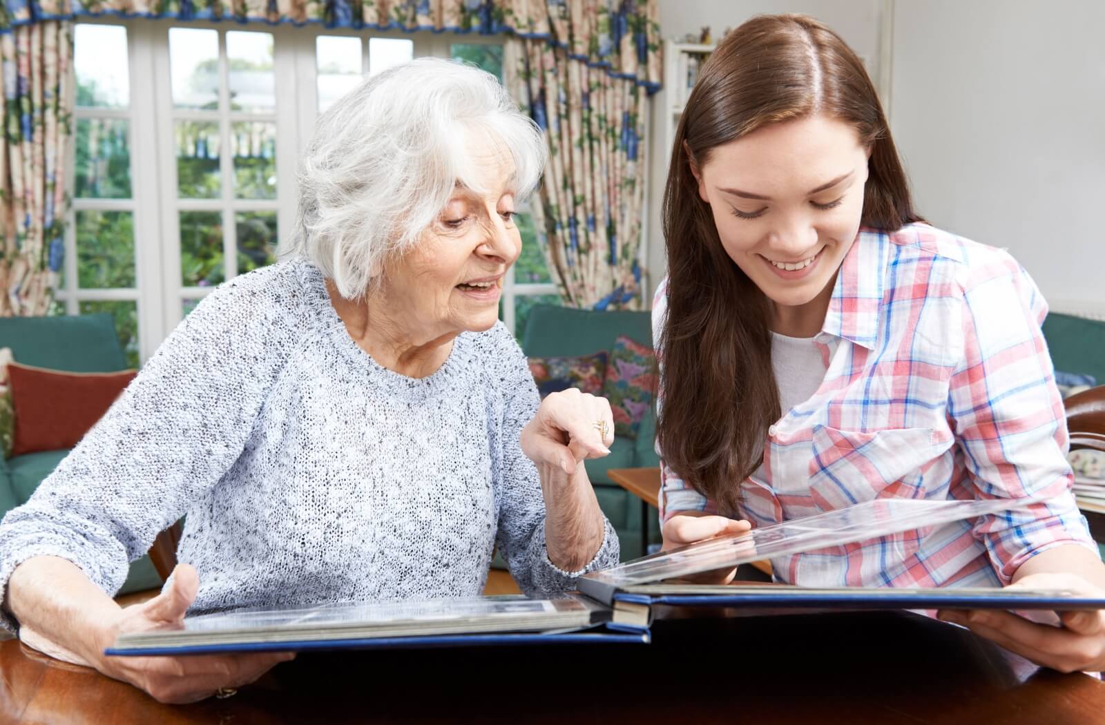 A grandparent and grandchild reminisce while looking through a photo album in a memory care community.