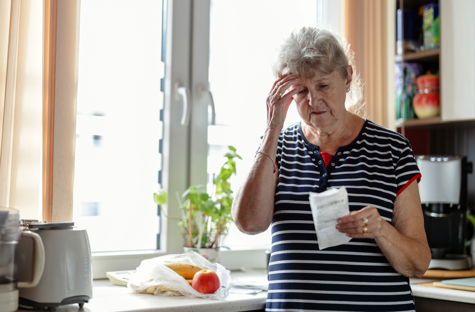 A senior in the early stages of dementia looks at a grocery receipt in confusion after coming home with not enough food